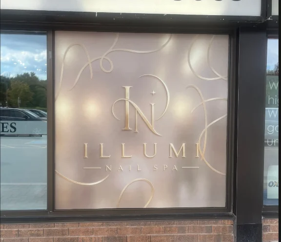 Illumi Nail Spa window graphic with a cream background, gold lettering and decorative gold lines.