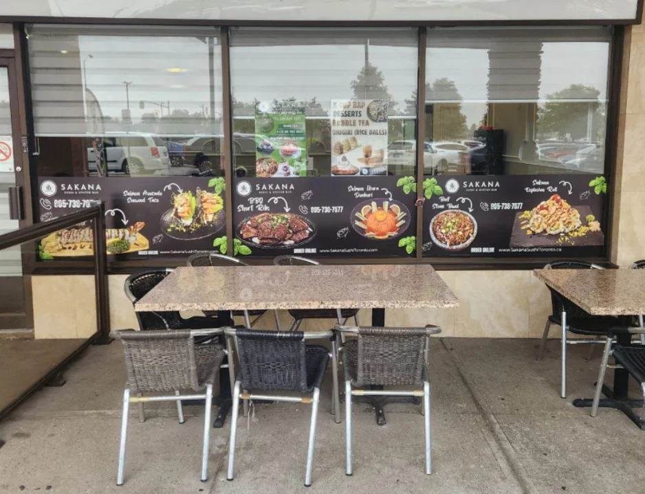 Sakana restaurant windows with lower-panel food graphics beside an outdoor patio.
